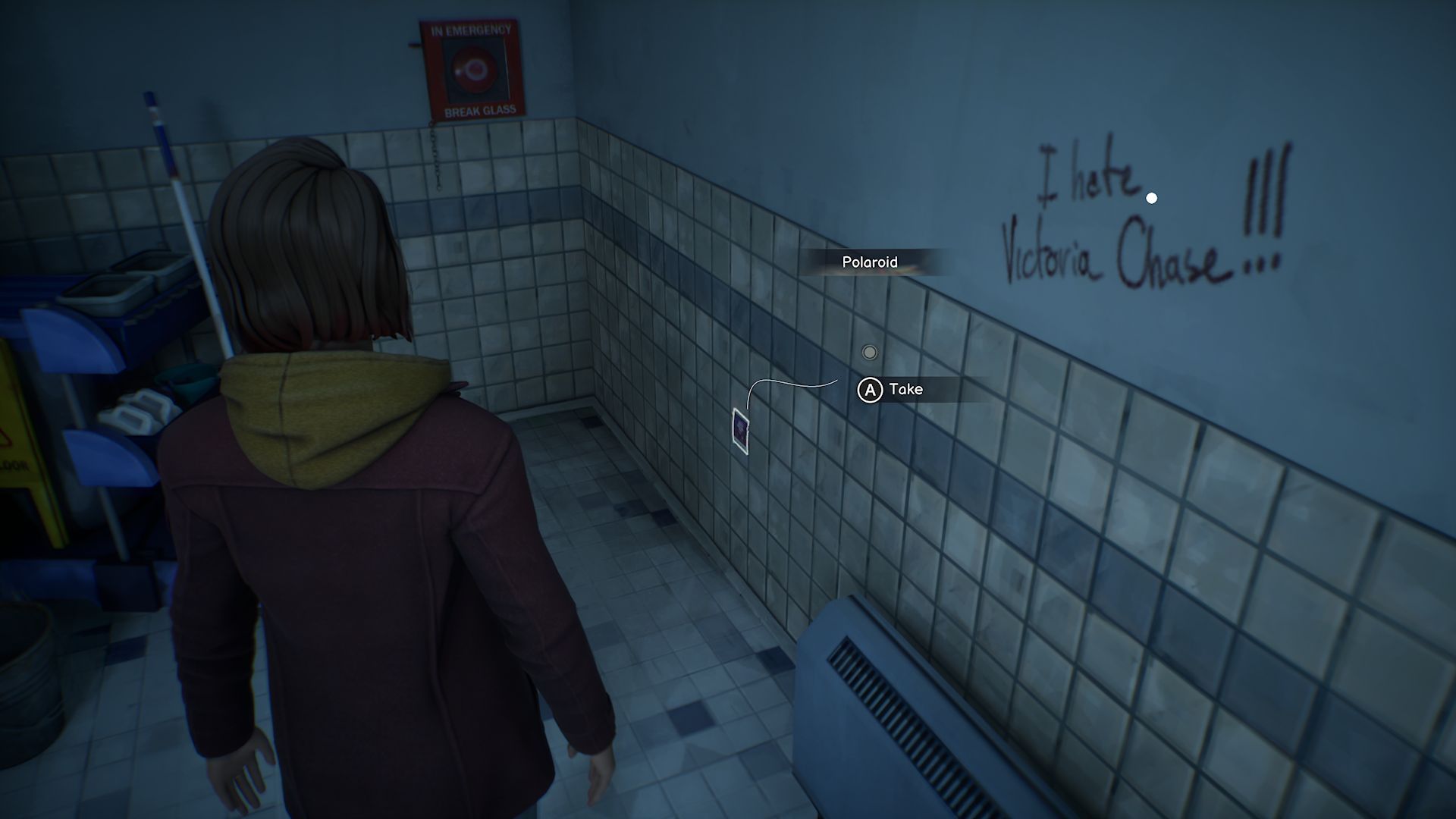 A screenshot with Max standing in front of the second Polaroid in Chapter 5, located on a bathroom wall near a corner, next to some graffiti.