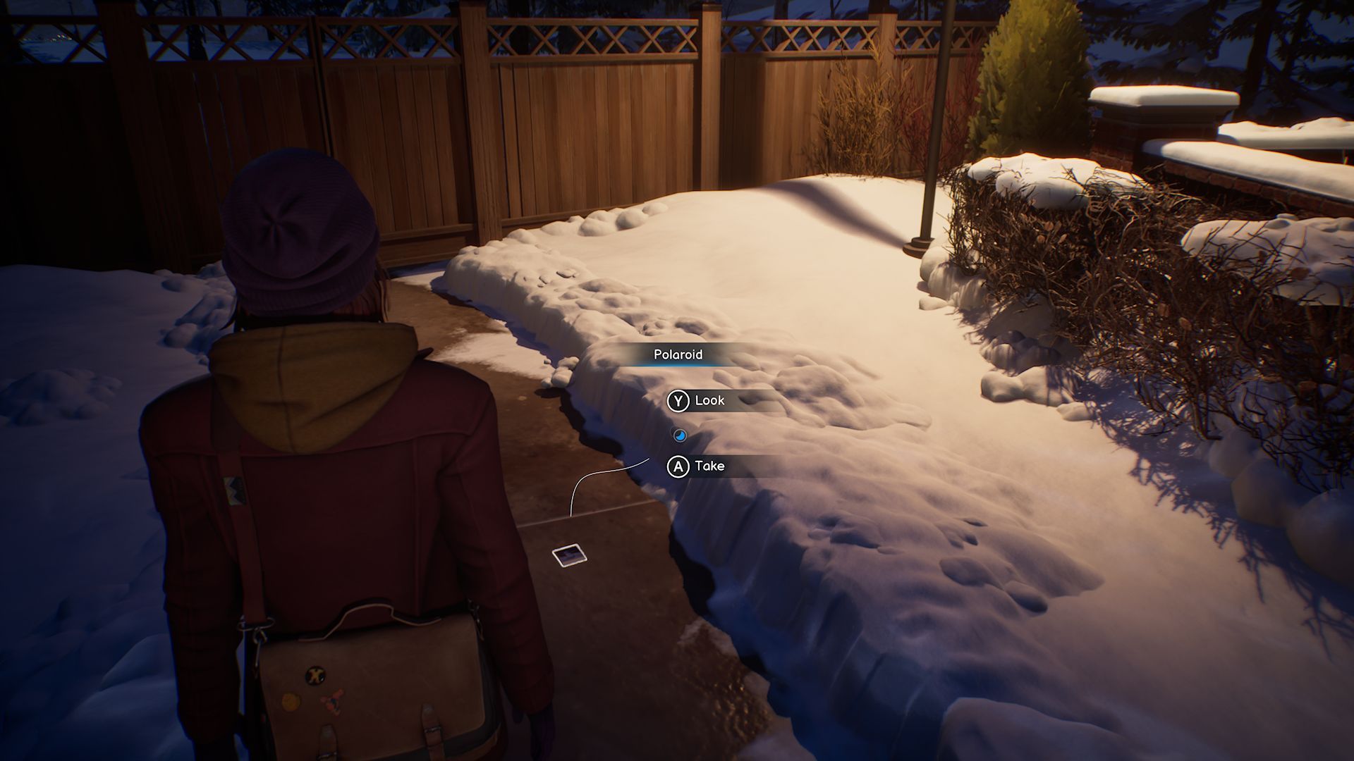 A screenshot with Max standing in front of the second Polaroid in Chapter 1, located on a stone path leading to a fence, surrounded by snow.